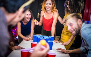 Young friends playing beer pong at youth hostel - Free time travel concept with backpackers having unplugged fun at guesthouse - Happy people on playful genuine attitude - Vivid vignetting filter